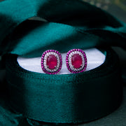 A pair of sterling silver earrings with a vibrant red gemstone centerpiece, displayed on a white surface with a green velvet background.